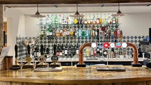 A bar area with a stone counter, multiple taps, and a variety of bottles in the background.
