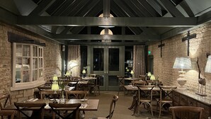 A restaurant with a rustic interior, featuring exposed brick walls, wooden tables and chairs, and a large, ornate chandelier hanging from the ceiling.