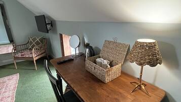 Een eetgedeelte met een houten tafel, stoelen, een mand met mokken, een lamp en een spiegel aan de muur.