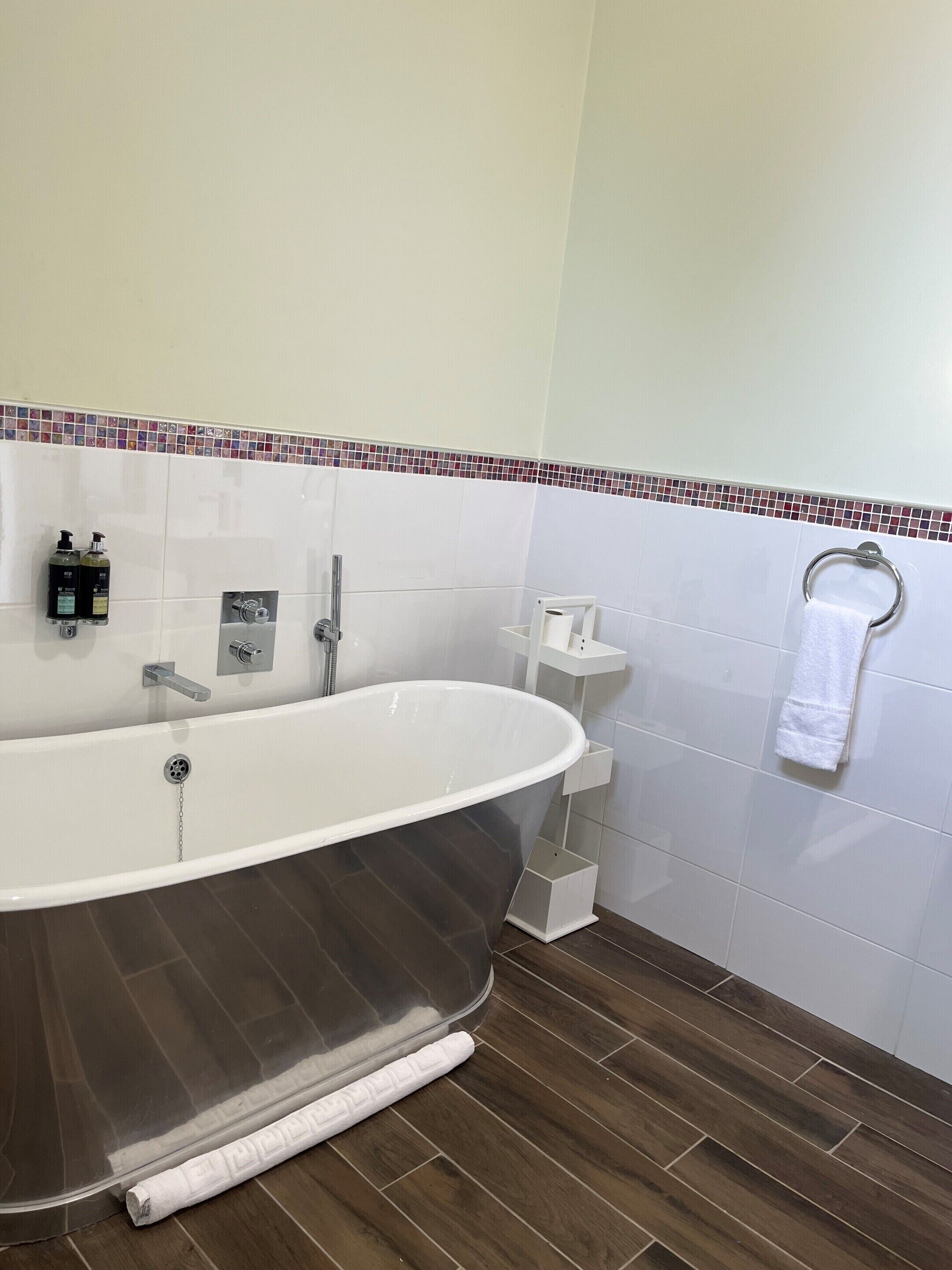 A modern bathroom with a freestanding bathtub, a towel rack, and a small shelf with toiletries.