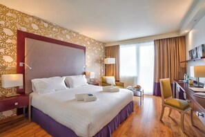 Habitación de hotel con una cama grande, dos mesitas de noche con lámparas, un escritorio con una silla y un televisor en la pared.