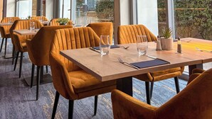 Ein Restaurant mit Tischen, Stühlen, großen Fenstern und Blick ins Freie.