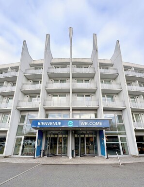 Un edificio de varios pisos con un letrero que dice 'BIENVENUE', ventanas amplias y un diseño arquitectónico moderno.