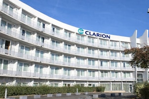 Un hotel de varios pisos con un llamativo letrero 'CLARION', balcones y un patio ajardinado.