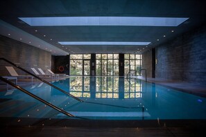 Une piscine intérieure avec de grandes fenêtres donnant sur la verdure, un escalier et un poste de surveillance pour les sauveteurs.