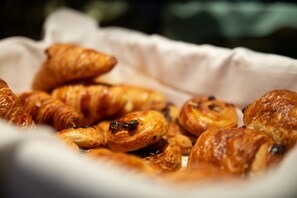 Una cesta con varios pasteles, incluyendo croissants y muffins, sobre una superficie blanca.