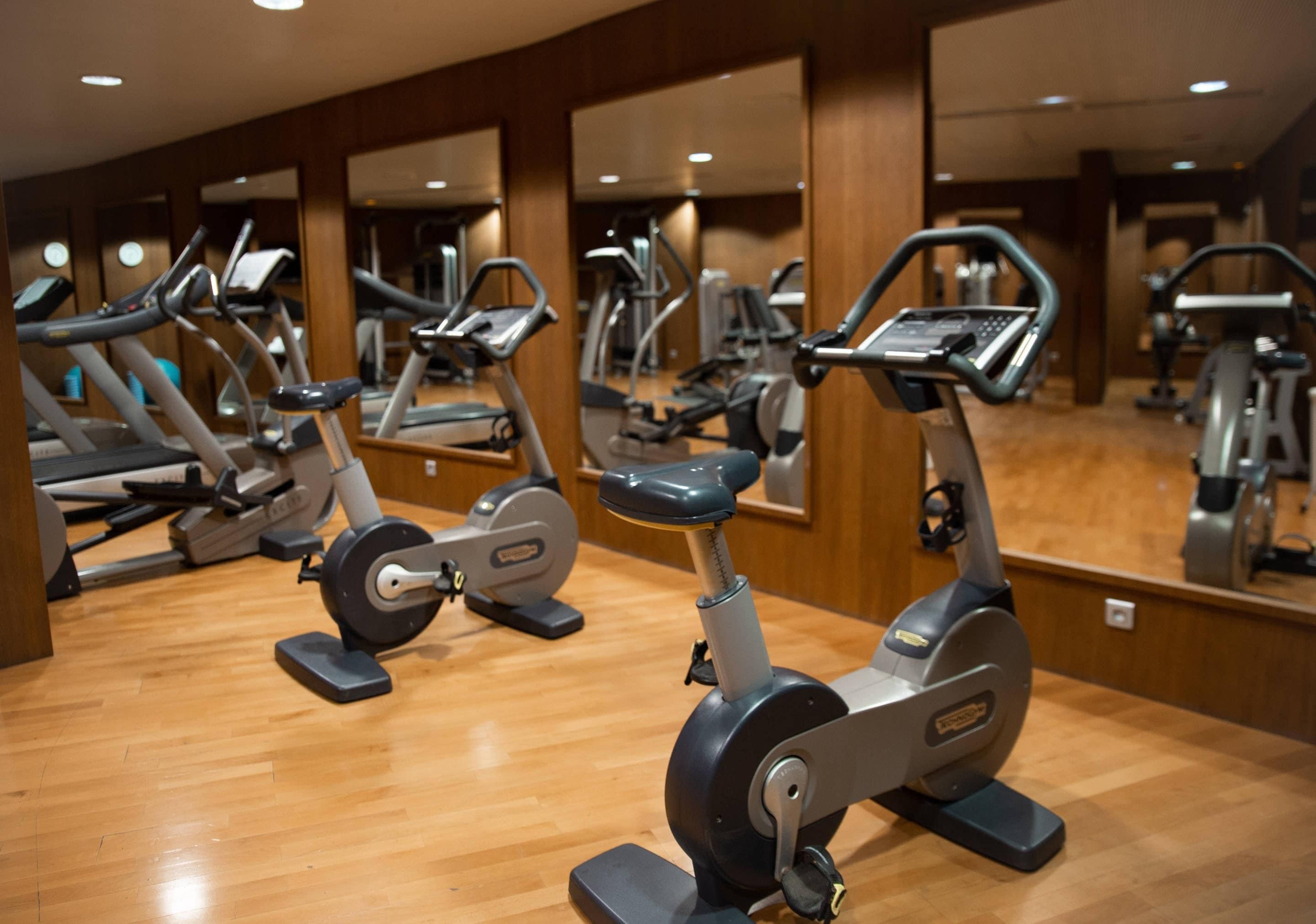 A gym with stationary bikes, mirrors, wooden flooring, and a wooden wall.
