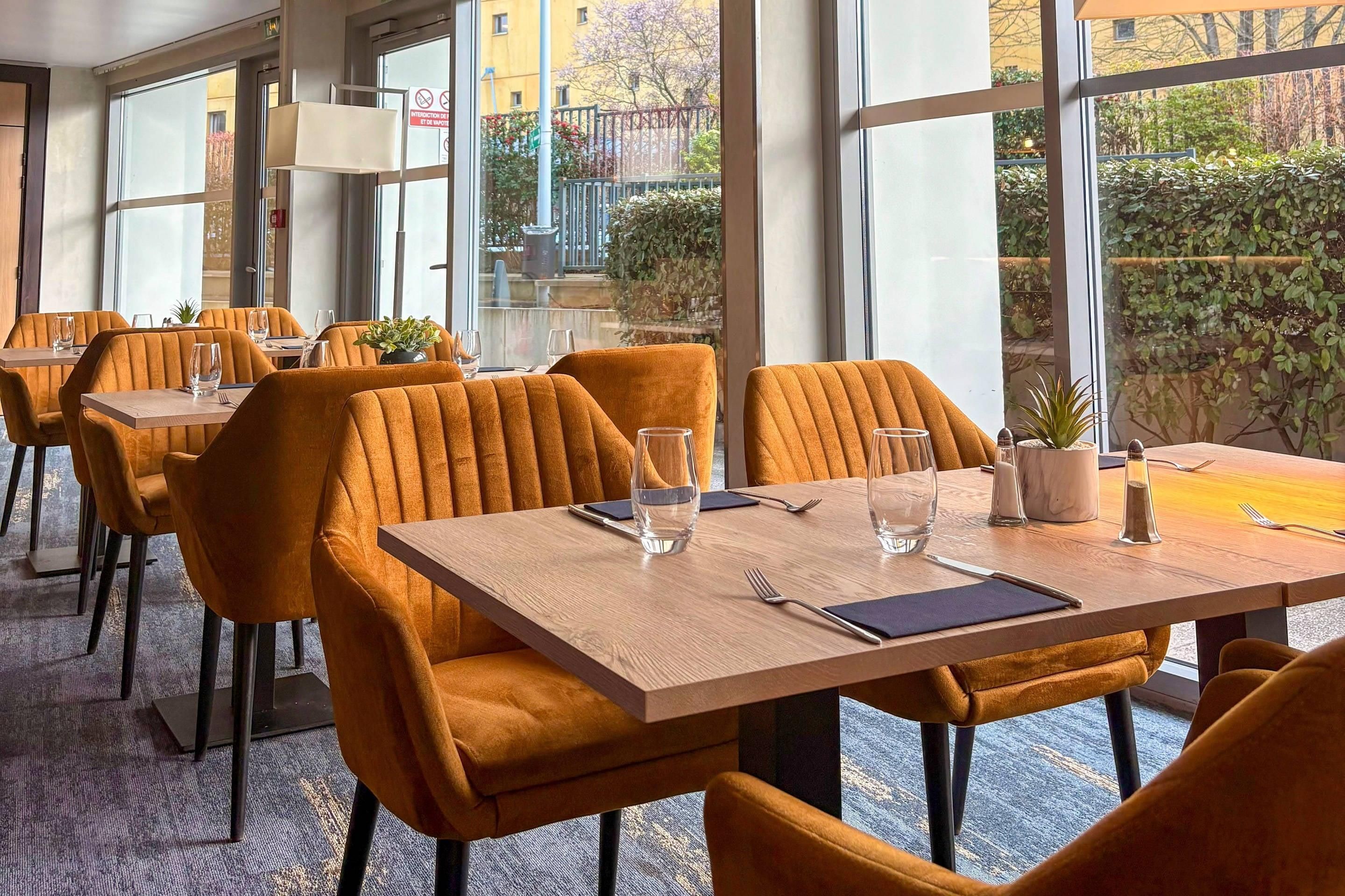 Un ristorante con sedie rivestite in arancione, tavoli in legno e ampie finestre che offrono vista all'esterno.