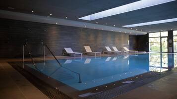 Une piscine intérieure au design moderne, dotée d’une verrière, de chaises longues et d’un sol carrelé.