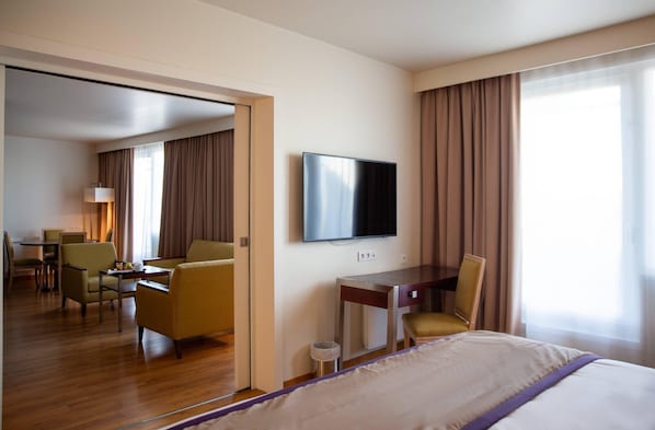 A hotel room with a bed, a desk, a chair, a television, and a dining area.