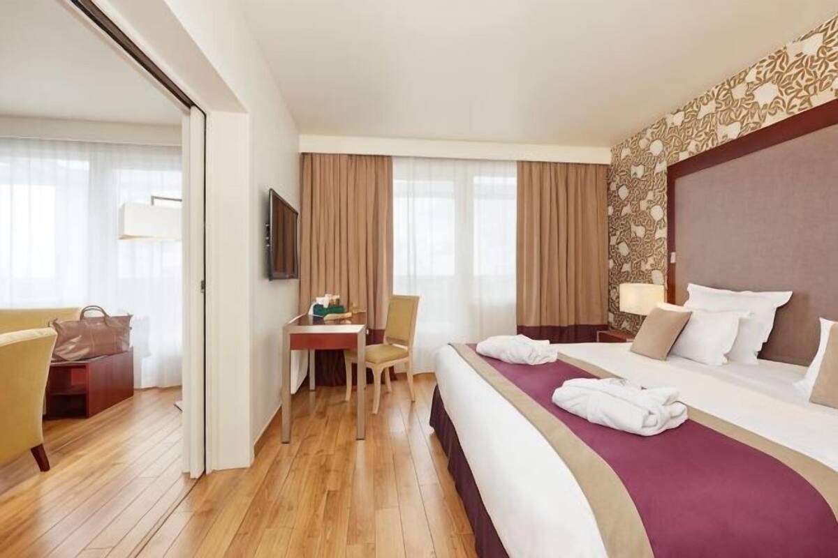 Ein Hotelzimmer mit Bett, Schreibtisch, Sessel und Fernseher mit Blick nach draußen.