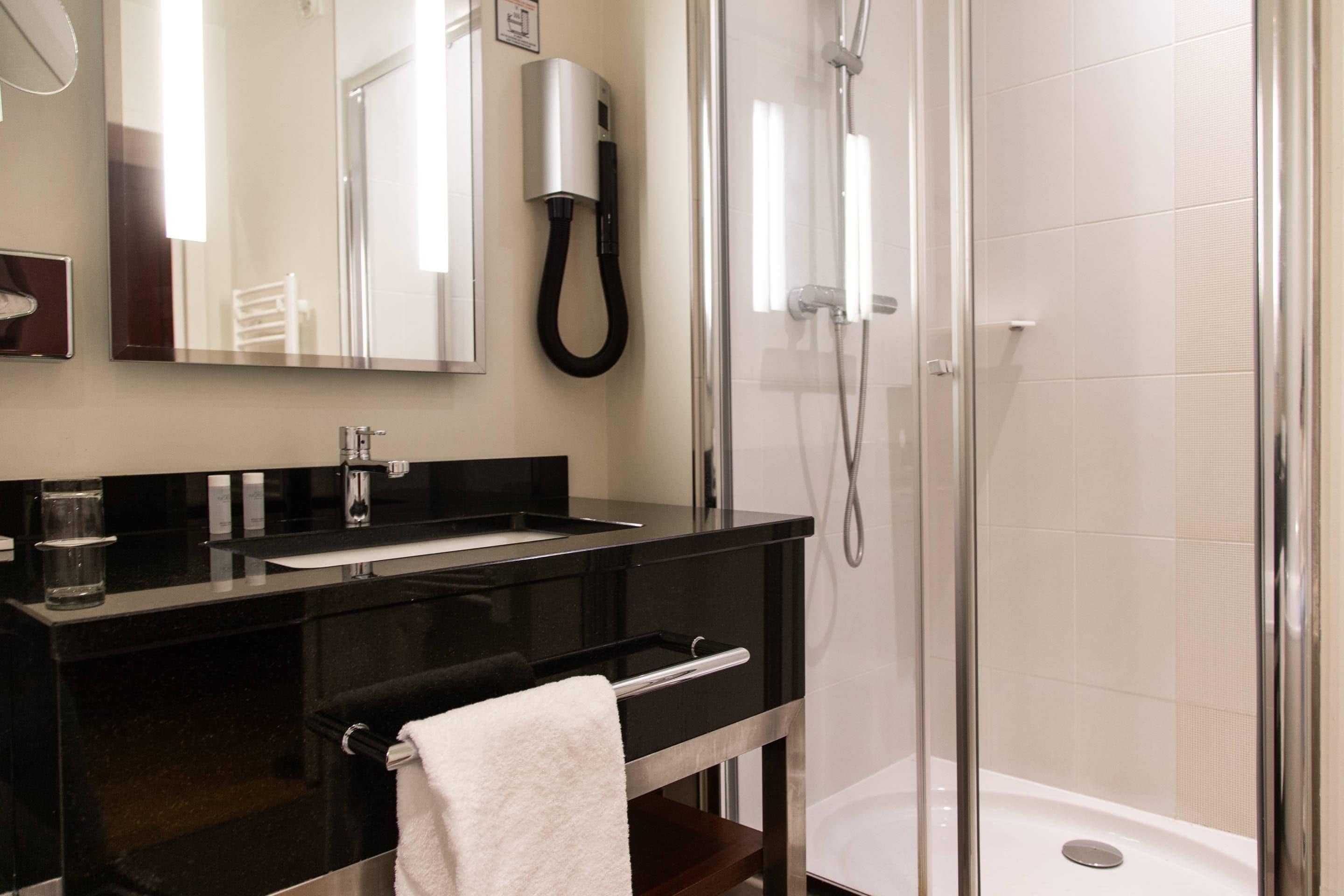 A modern bathroom with a black vanity, a glass shower enclosure, and a white towel on the counter.