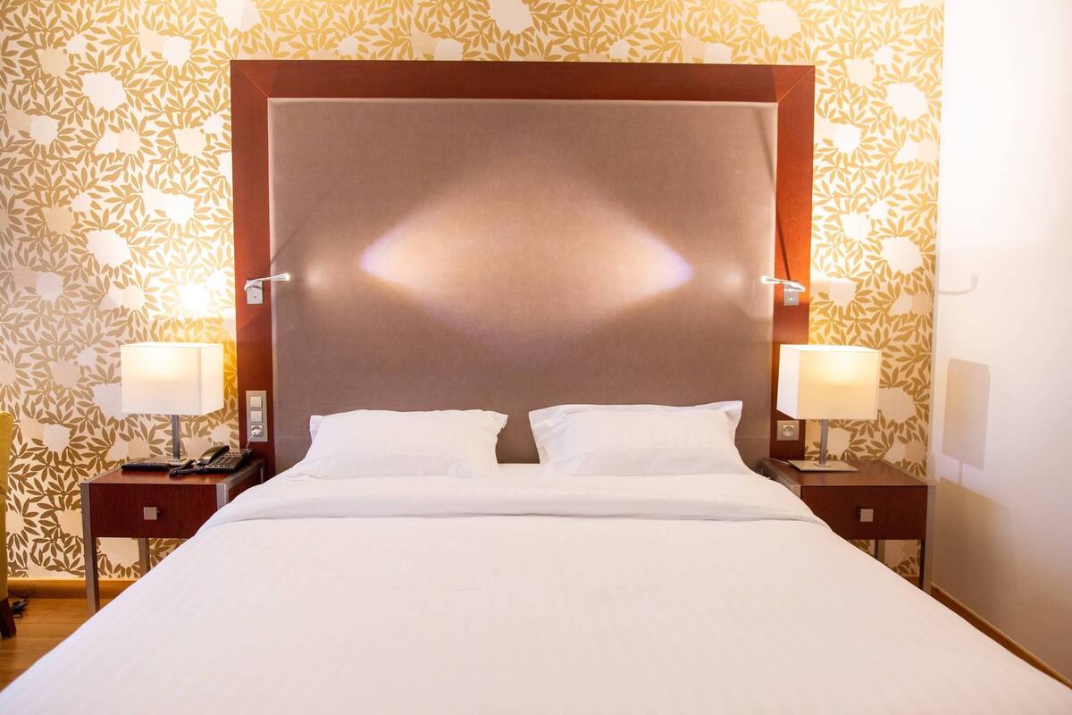 Une chambre d’hôtel avec un grand lit, deux tables de chevet avec des lampes et un papier peint à motifs.
