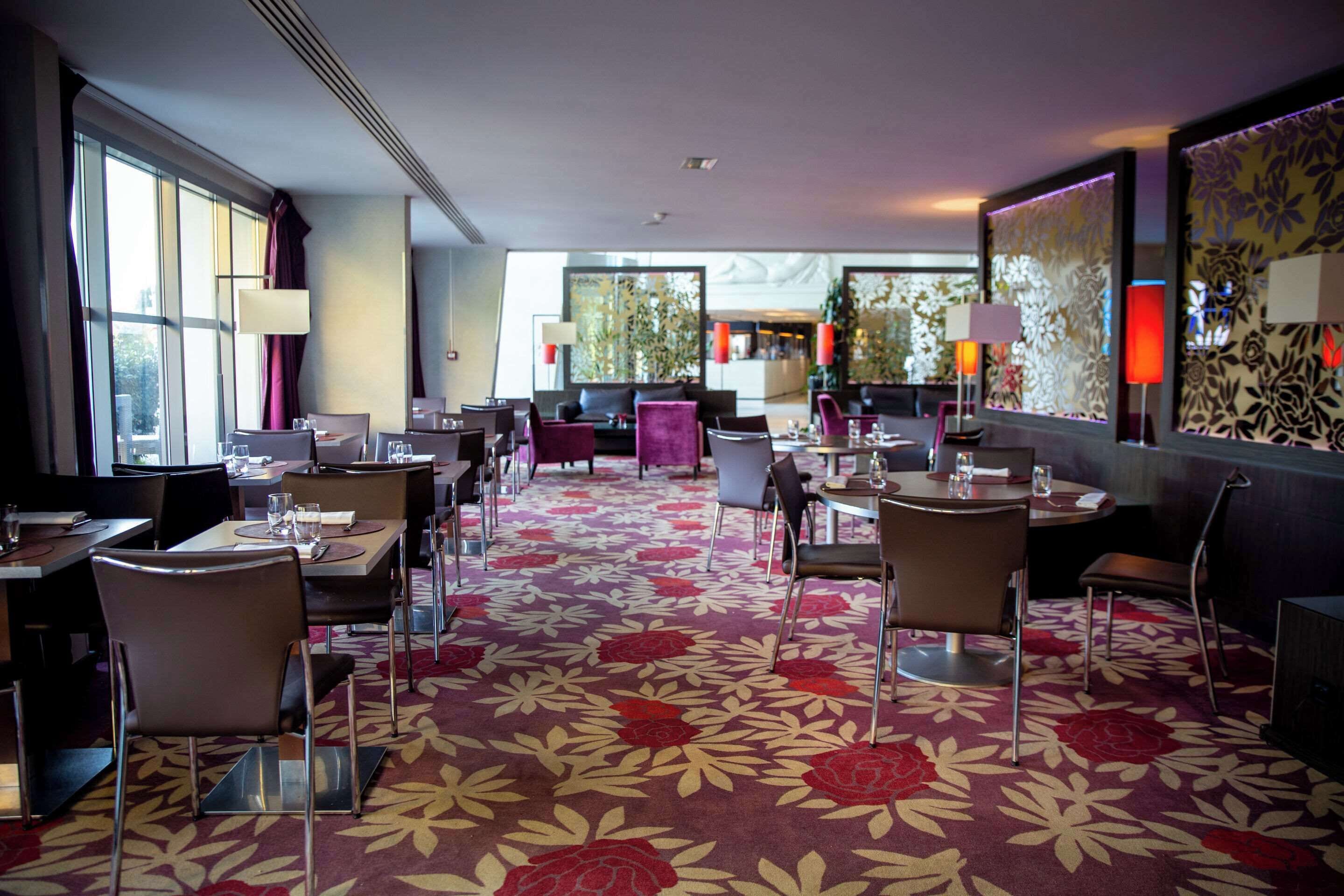 Ein Hotel-Essbereich mit Tischen, Stühlen und einem gemusterten Teppich.
