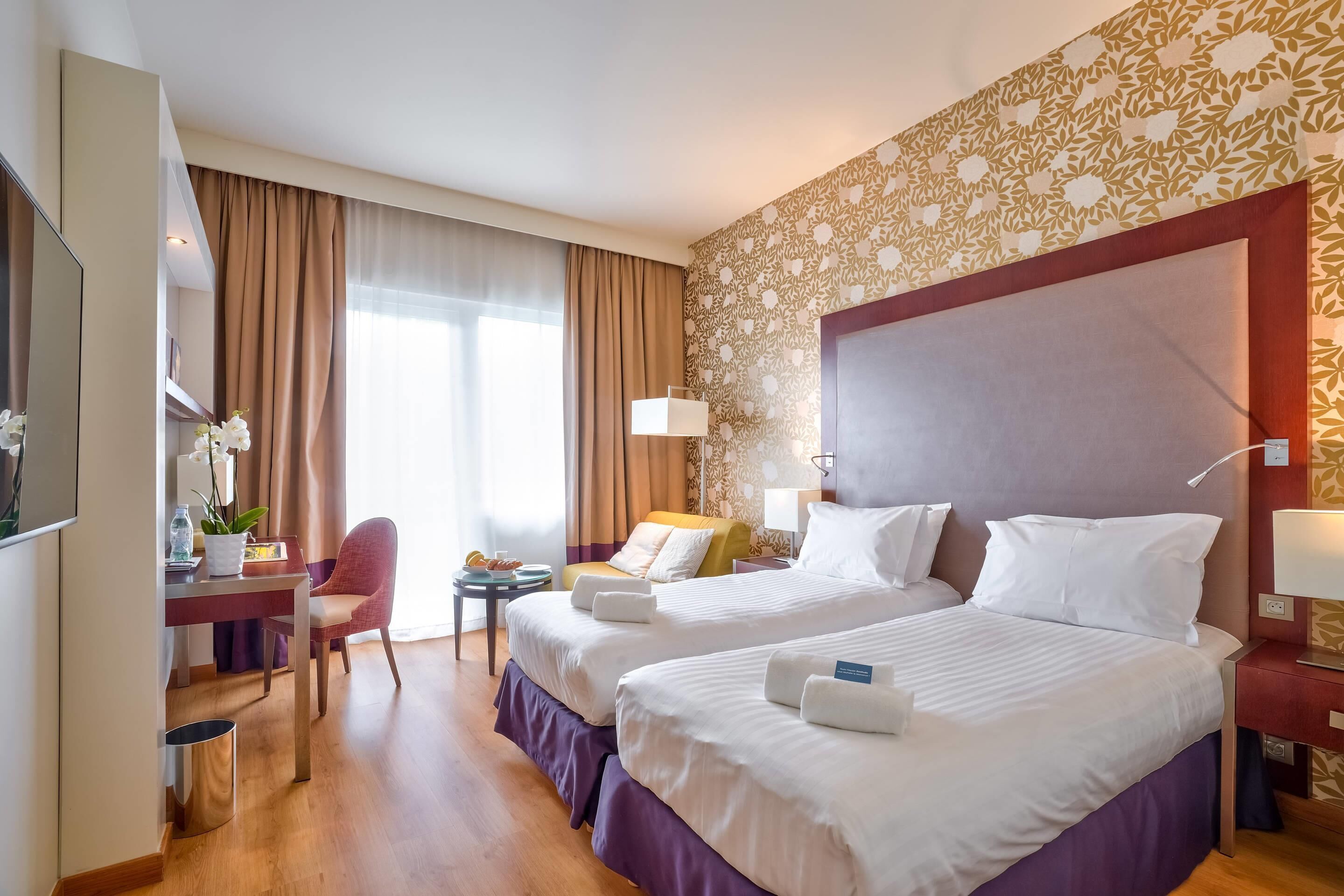 Une chambre d’hôtel avec deux lits, un bureau, une chaise et une petite table.