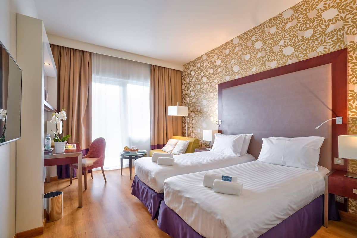 Une chambre d’hôtel avec deux lits, un bureau, une chaise et une petite table.