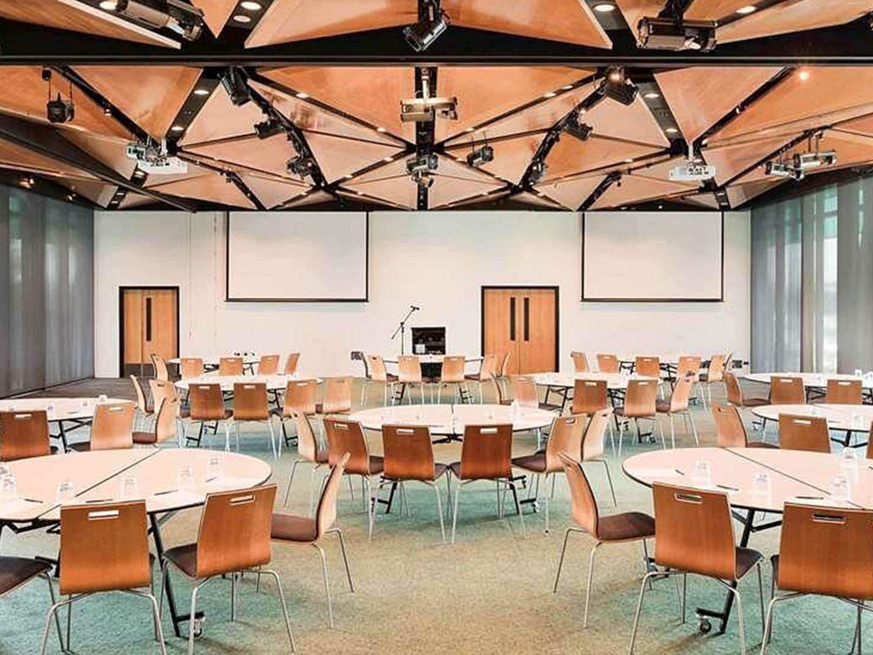 A conference room with multiple tables and chairs, equipped with projectors and a podium.