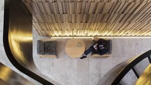 A modern interior with a curved metallic structure, a wooden slatted ceiling, and a person sitting on a bench. - Novotel Auckland Airport (Auckland)