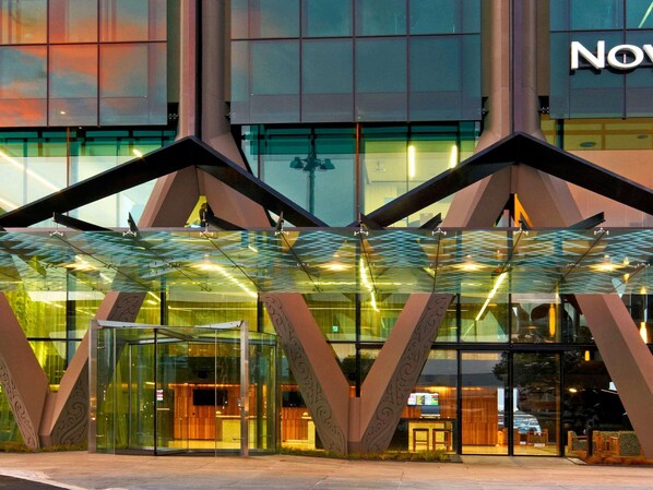 A modern hotel entrance with a glass facade, geometric architectural design, and a visible reception area. - Novotel Auckland Airport (Auckland)