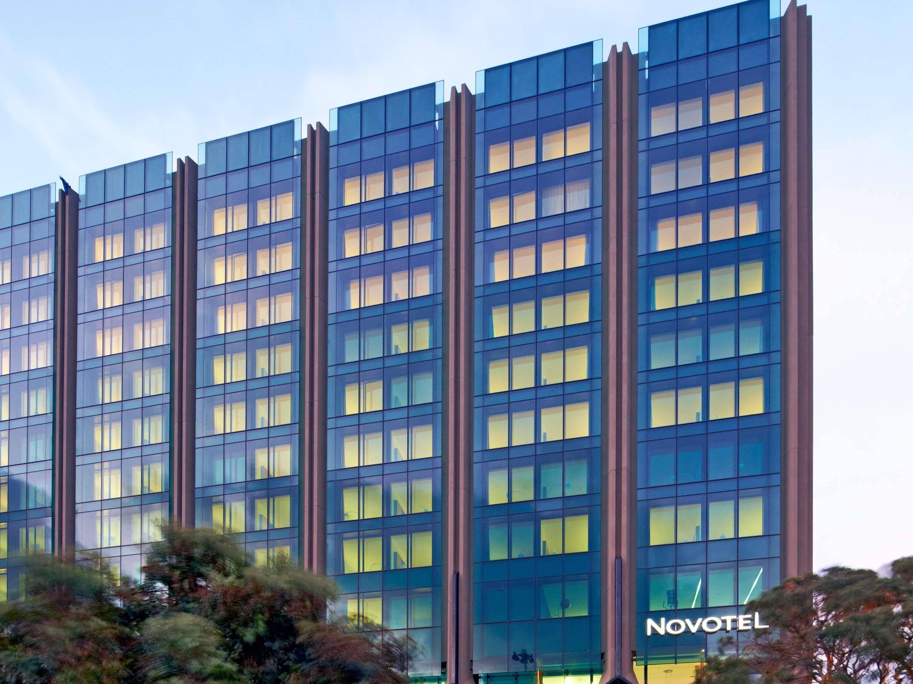A high-rise hotel with a modern glass facade, multiple floors, and a prominent 'Novotel' sign.