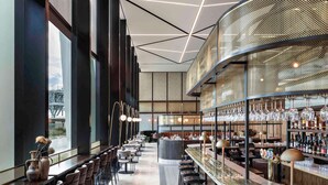 A modern bar area with high stools, a bar counter, and a view of a bridge outside. - Novotel Auckland Airport (Auckland)