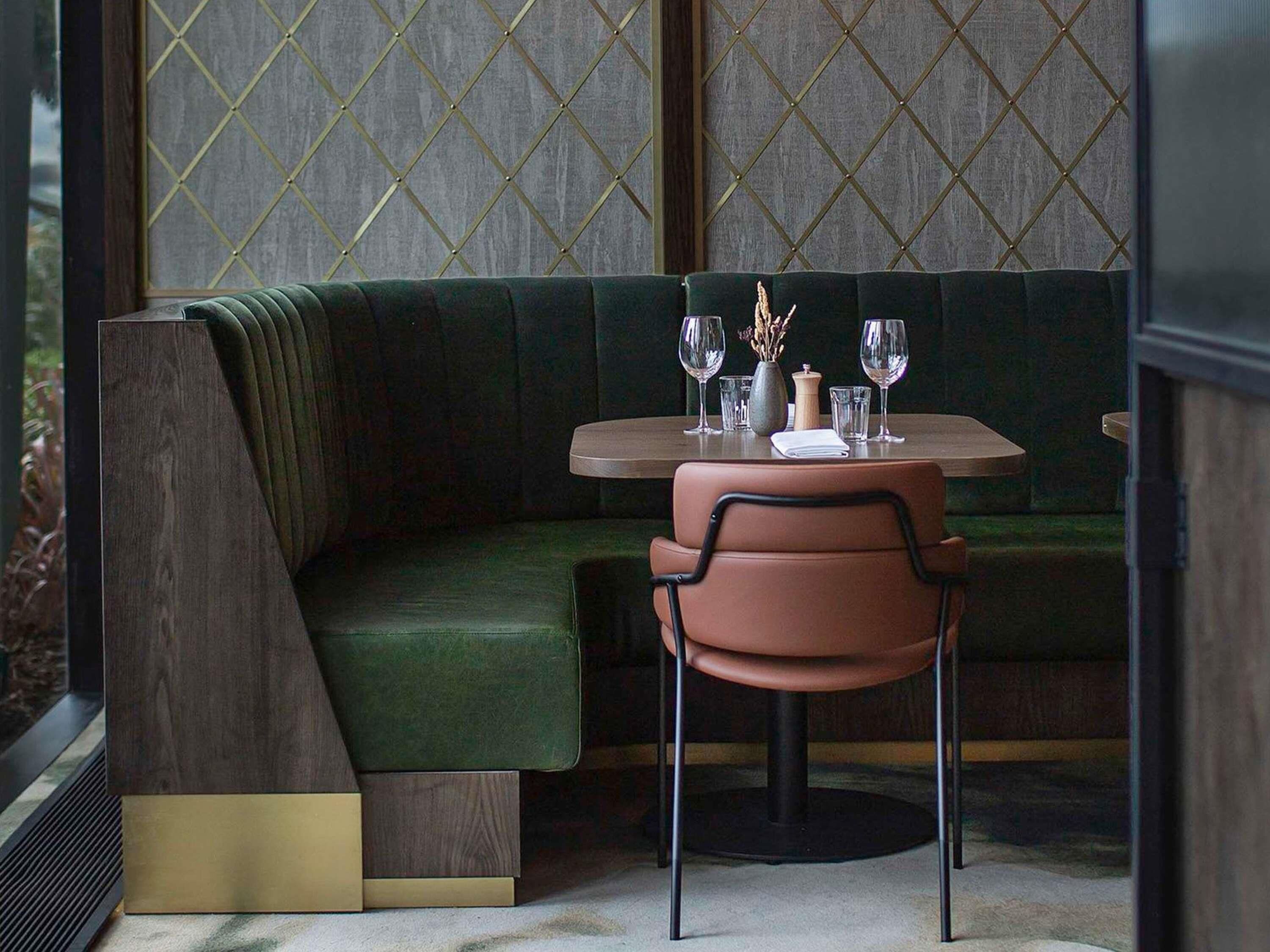 Un comedor moderno con un banco acolchado verde, una mesa redonda y una silla.