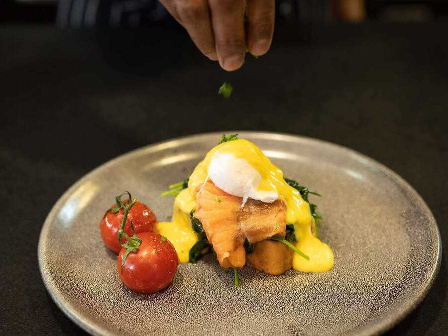 A plate with a poached egg, smoked salmon, and hollandaise sauce, garnished with a sprig of parsley.