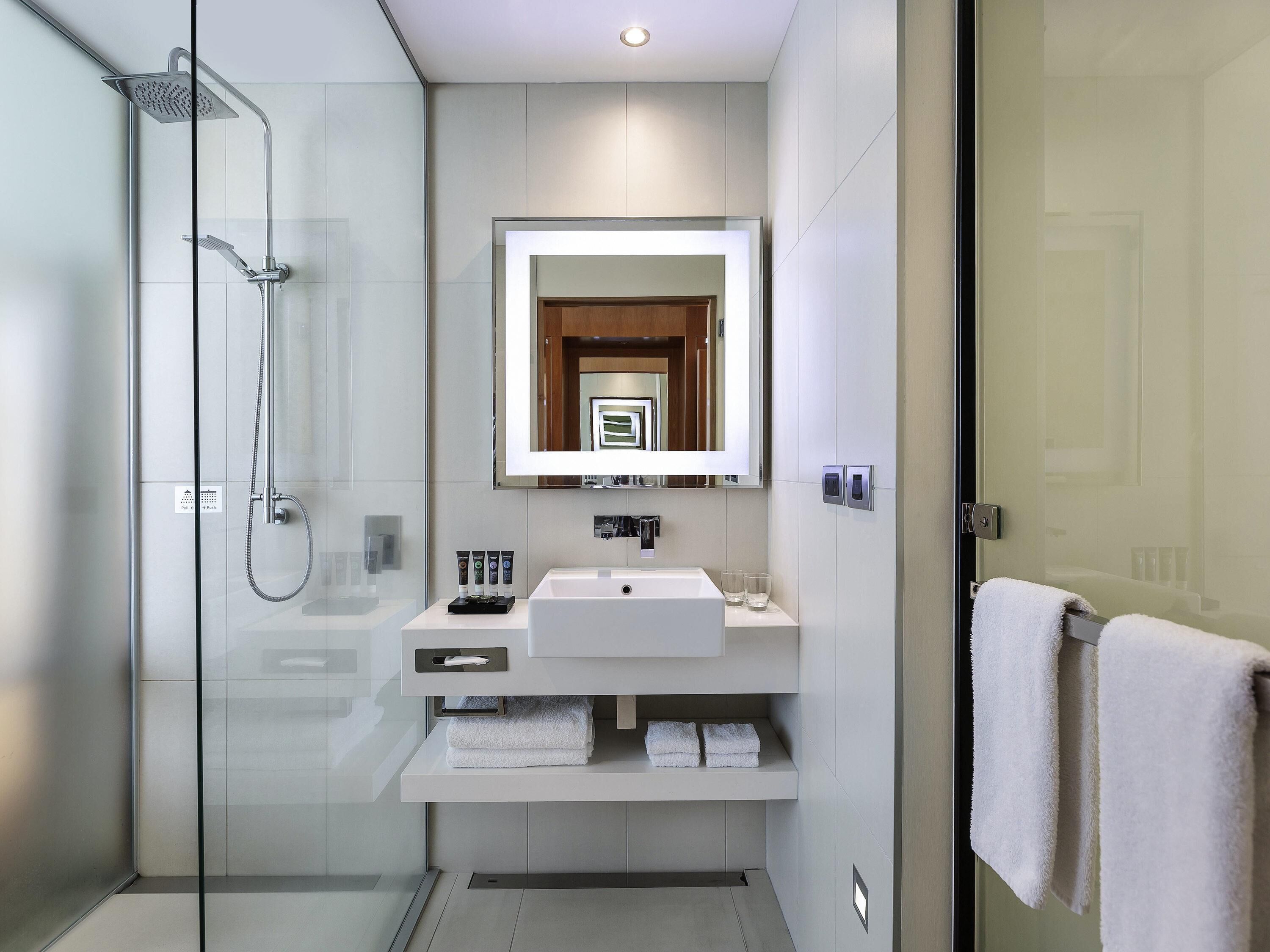 Un baño moderno con ducha de vidrio, un lavamanos blanco y un espejo encima.
