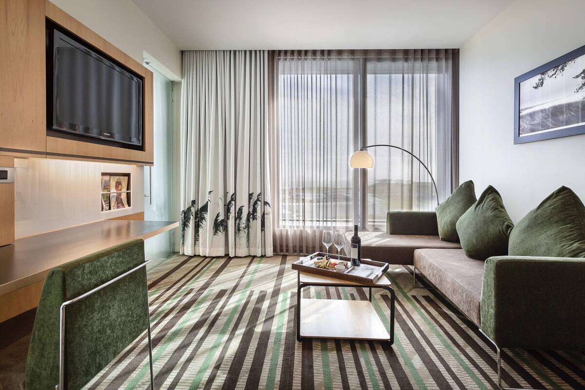 A modern hotel room with a flat-screen TV, a sofa, a coffee table, and a striped carpet.