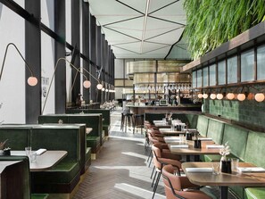 A restaurant interior with booths, tables, hanging lights, and a bar area. - Novotel Auckland Airport (Auckland)