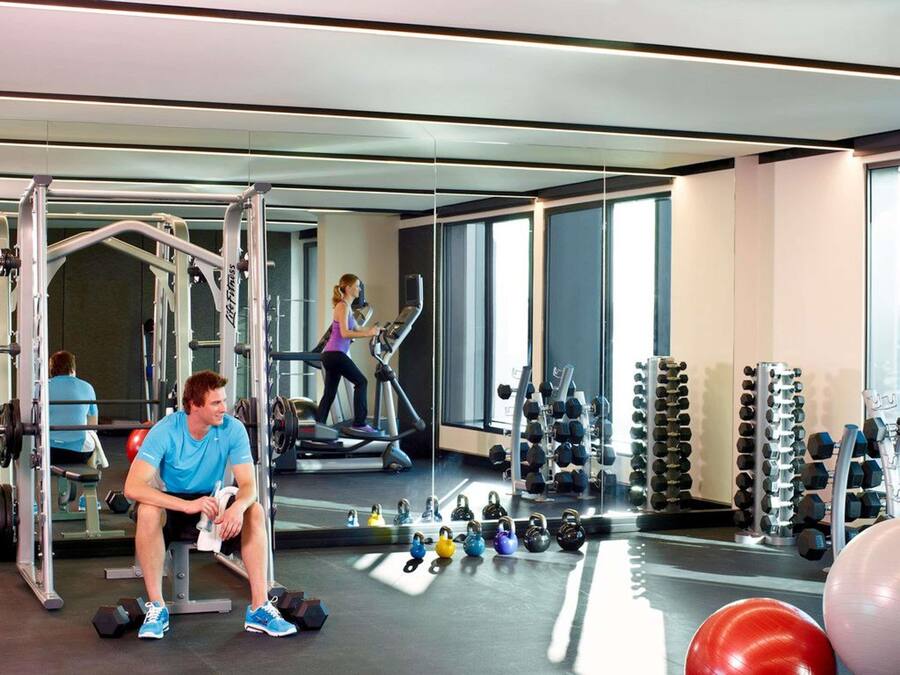 A gym with exercise equipment, a seated individual, and a person using a treadmill.