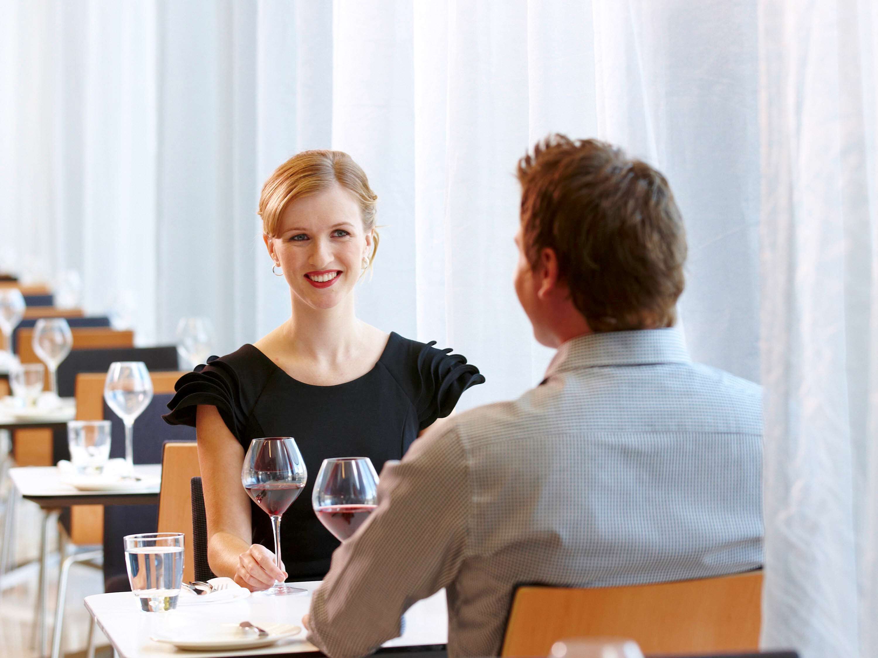 A dining area with tables set for two, glasses of wine, and a waiter attending to guests.