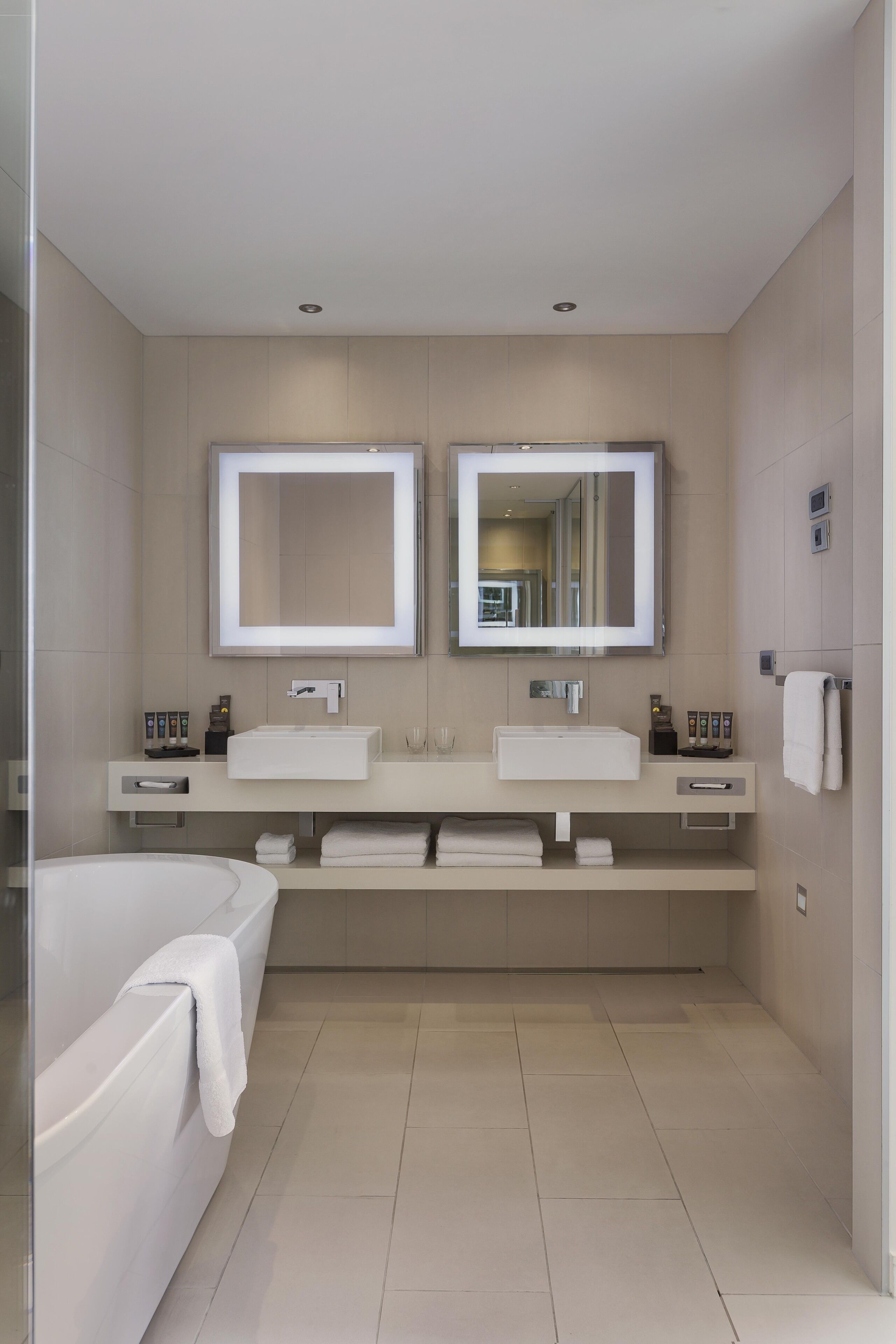 Un baño moderno con dos lavamanos, un espejo grande, una bañera y una cabina de ducha con mampara de vidrio.
