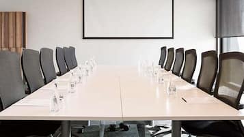 A conference room with a long table, chairs, a projector screen, and a carpeted floor.