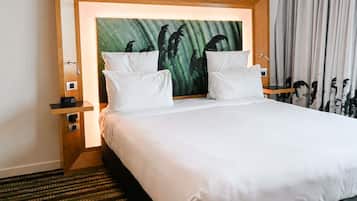 A hotel room with a large bed, two white pillows, a headboard with a tropical painting, a nightstand with a clock, and a window with curtains.
