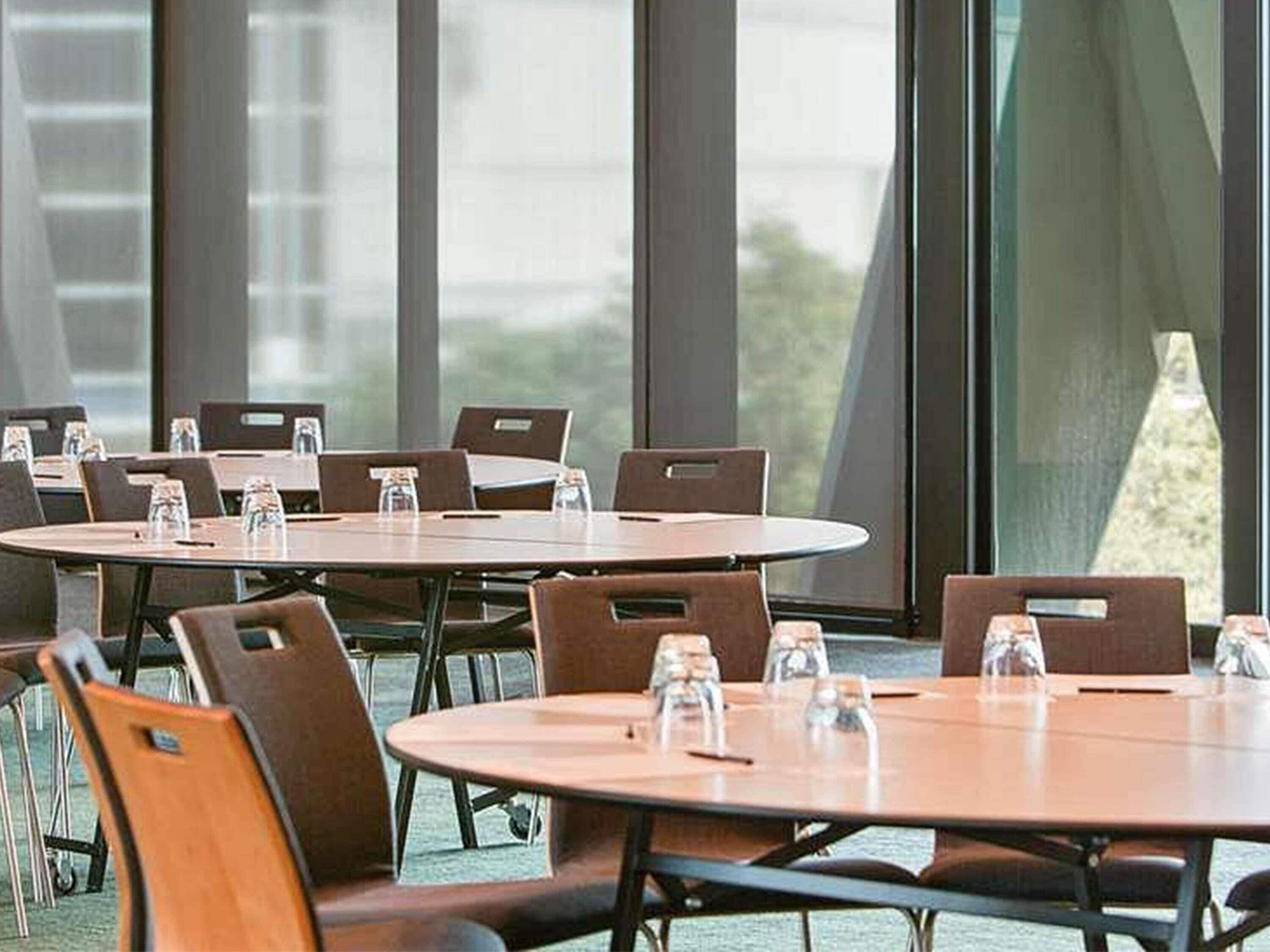 A conference room with round tables and chairs, large windows, and water bottles on the tables.