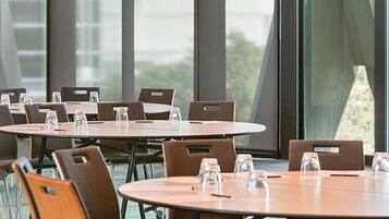 A conference room with round tables and chairs, large windows, and water bottles on the tables.