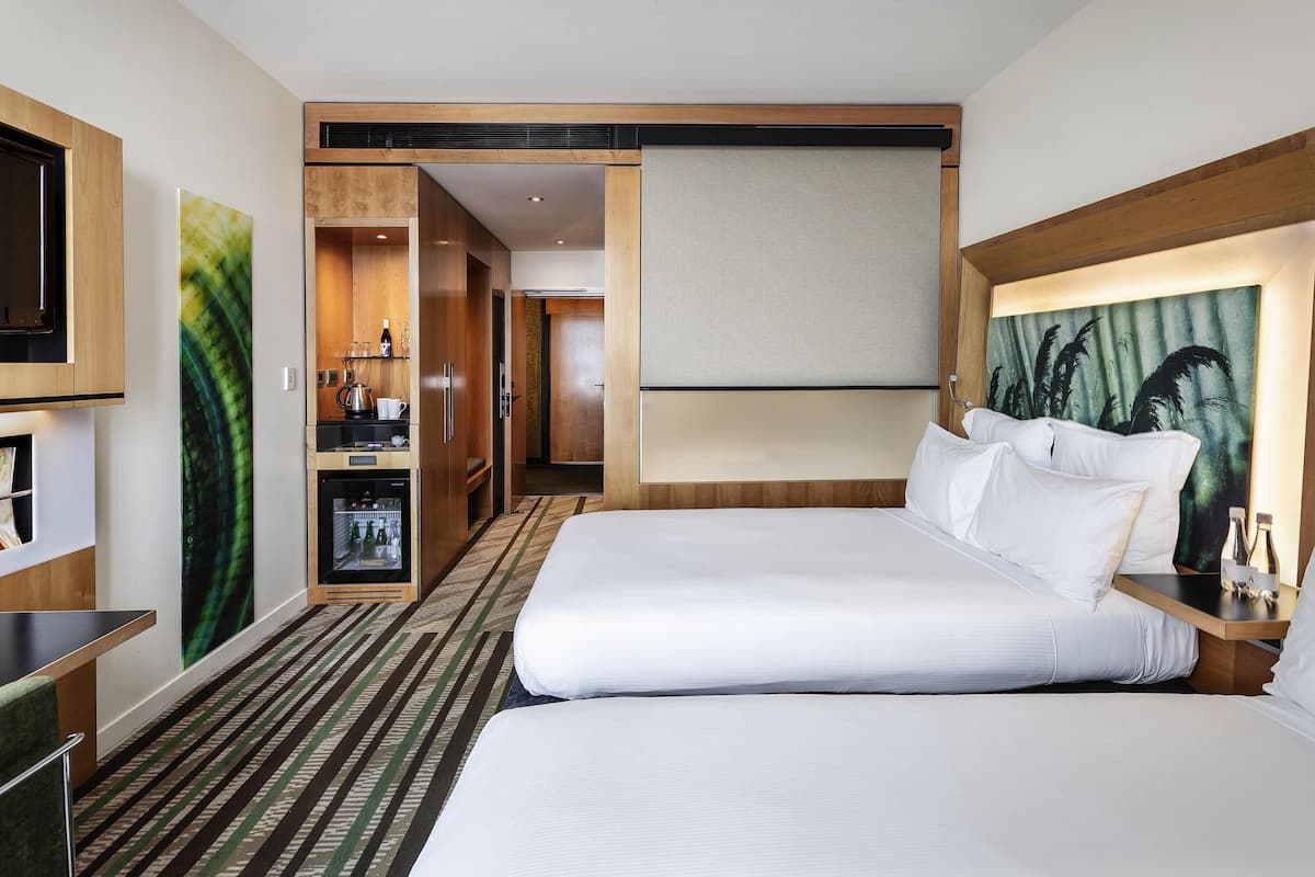 A hotel room with a bed, a desk, a minibar, a television, and a painting on the wall.