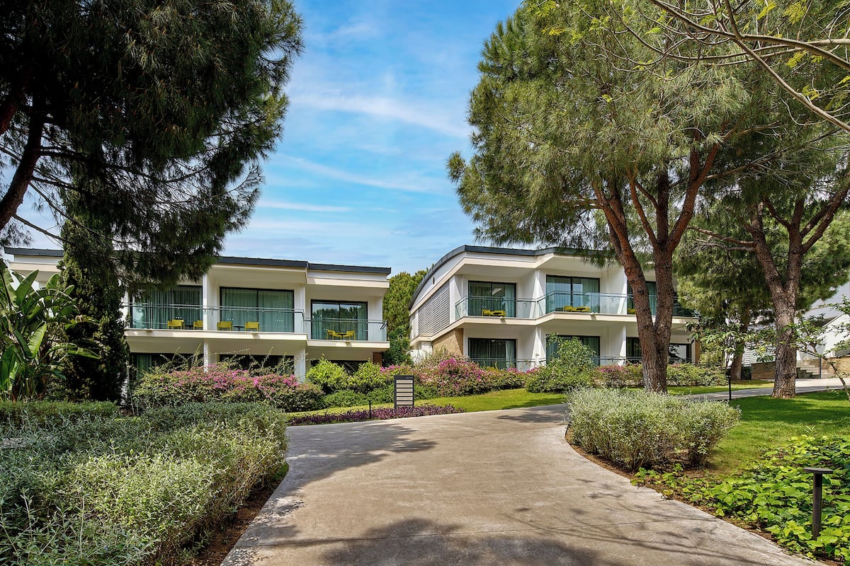 A modern building with a pathway leading to the entrance, surrounded by well-maintained greenery and trees.