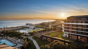 A resort with a pool, a large building with multiple floors, and a view of the ocean at sunset. - Voyage Belek Golf & Spa (Serik)