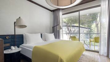 A hotel room with a bed, bedside lamps, a telephone, a small table, and a view of the outdoors through large windows.