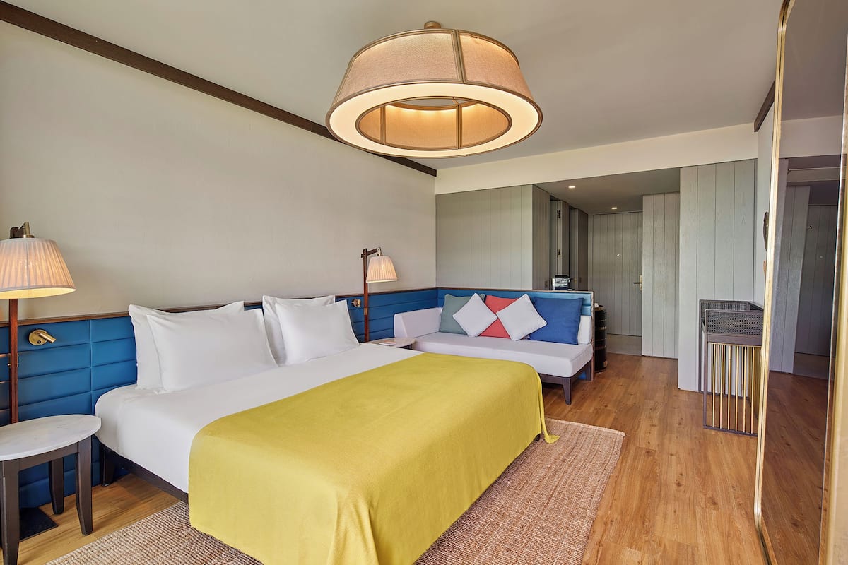 A hotel room with a large bed, a bedside table, a lamp, a mirror, and a view of the hallway.