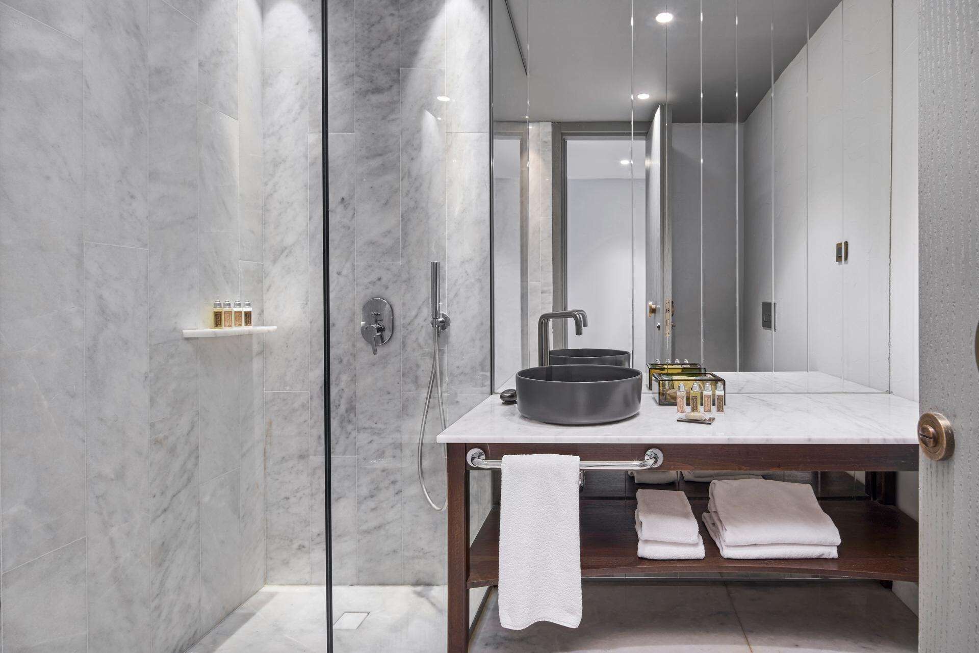 Un baño moderno con ducha envuelta en vidrio, tocador de mármol y un perchero para toallas.