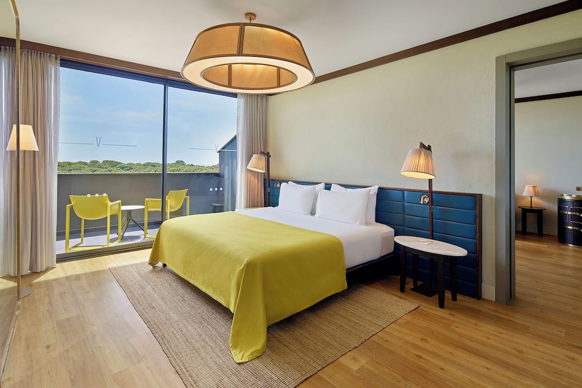 A hotel room with a large bed, a small table, a chair, and a view of the outdoors.
