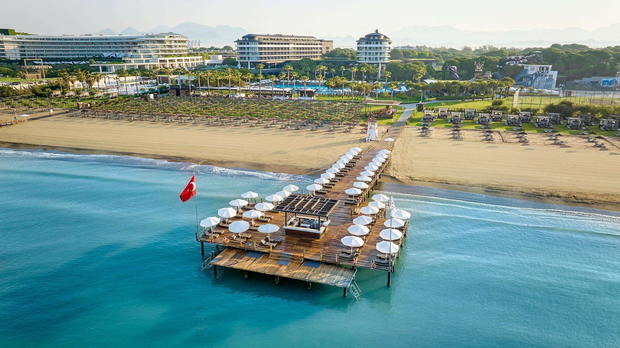 Hotel amb vistes al mar i un embarcador que s'endinsa a la mar, amb gandules i ombrel·les.