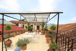 A covered patio area with a table and chairs, surrounded by potted plants and a view of a building with a tiled roof. - Mansión de los Ángeles (San Cristóbal de las Casas)