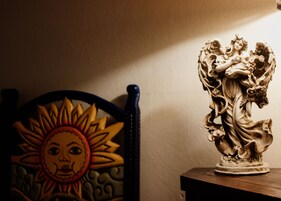 Une statue d’un ange sur un piédestal, une chaise ornée d’un motif solaire et un mur en arrière-plan.