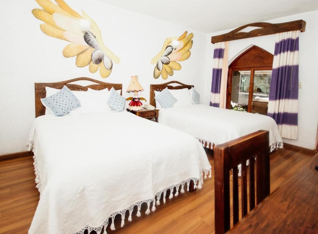 Une chambre avec deux lits en bois, une table de chevet, une lampe et une fenêtre avec des rideaux.