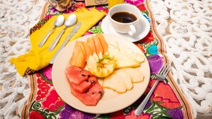 A breakfast setup with a plate of fruit, a cup of coffee, and a glass of orange juice on a colorful tablecloth.