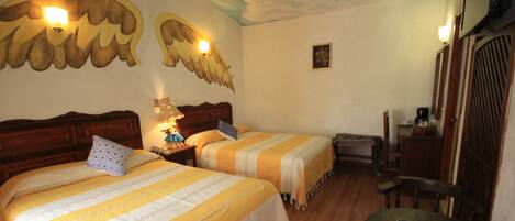 Quarto de hotel com duas camas, uma mesa pequena e um mural no teto.